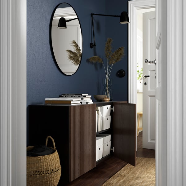 Entrée moderne avec armoire BESTÅ, portes ouvertes, stylisée avec des livres et de la décoration. Miroir mural et lumière au-dessus.