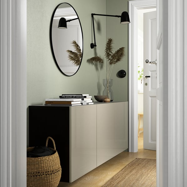 Couloir moderne avec buffet blanc BESTÅ, panier noir, miroir rond, appliques murales, fleurs d’herbe de la pampa et porte ouverte.