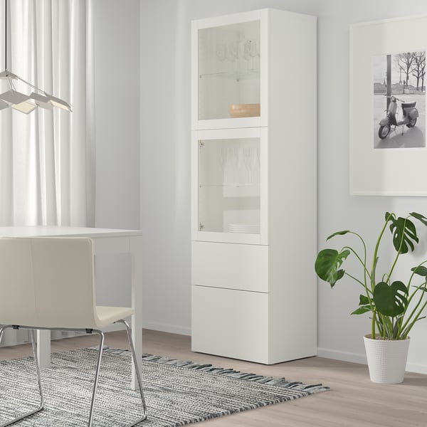 Armoire BESTÅ blanche avec portes en verre, verrerie, chaise, tapis, plante, photo.