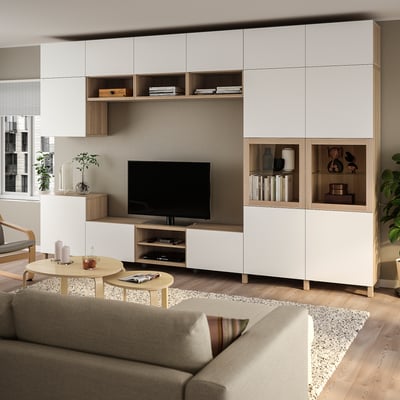 Salon moderne avec des meubles de rangement BESTÅ en bois blanc et clair. Grande section TV, portes vitrées et décor minimaliste.