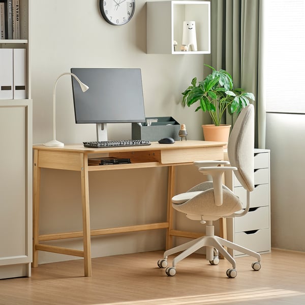 Petit bureau en bambou avec tiroir de rangement, chaise blanche et plante verte. Installation organisée de bureau à domicile avec écran, clavier et lampe.