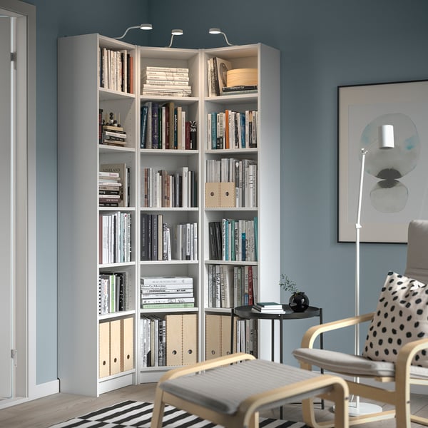 De grandes bibliothèques blanches BILLY remplissent un coin, dominant une table d’appoint noire et une petite chaise en bois avec un coussin à pois.