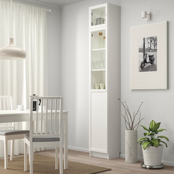 Salle à manger minimaliste avec armoire BILLY blanche exposant des articles, à côté d’une chaise et d’une table blanches sous une lampe suspendue.