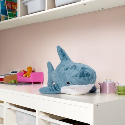 Peluche de requin bleu sur l’étagère avec des articles de maison de poupée.