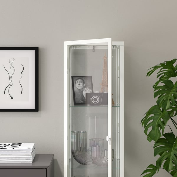 Armoire à portes vitrées avec étagères en verre, exposant des vases et une photo encadrée.