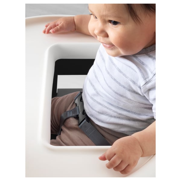 Bébé dans une chaise haute avec ceinture de sécurité, chemise rayée, pantalon marron.