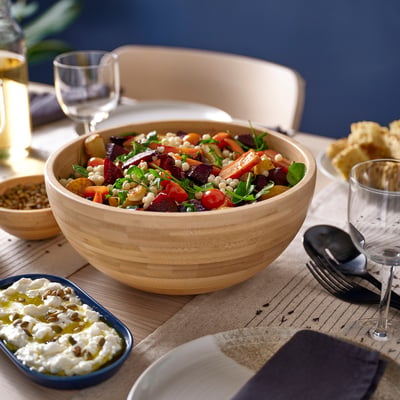 Un bol en bois rempli de salade colorée se trouve sur la table près de petits récipients avec des côtés et des verres.