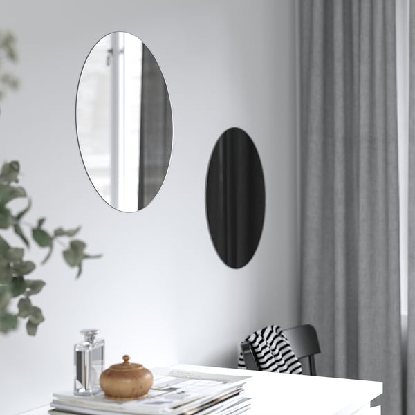 Deux miroirs ovales au mur ; L’un réfléchissant, l’autre noir, au-dessus de la table avec des objets décoratifs.