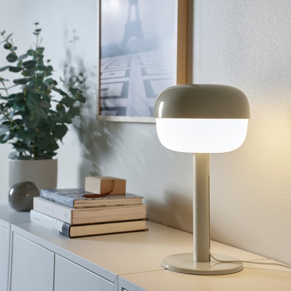Lampe de table moderne BLÅSVERK, lumière douce, design épuré. Teinte verdâtre, forme douce, petit, à côté de livres, plante, image.