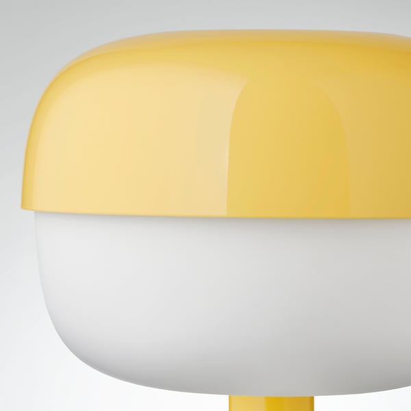 Lampe de table moderne jaune et blanche aux courbes douces, émettant une lumière douce.