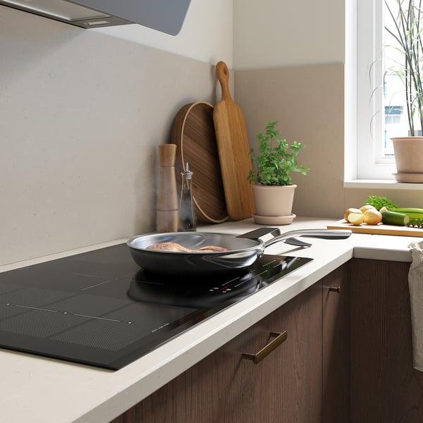 Cuisine moderne avec plaque de cuisson à induction noire élégante, ustensiles en bois, plantes et produits frais sur le comptoir.