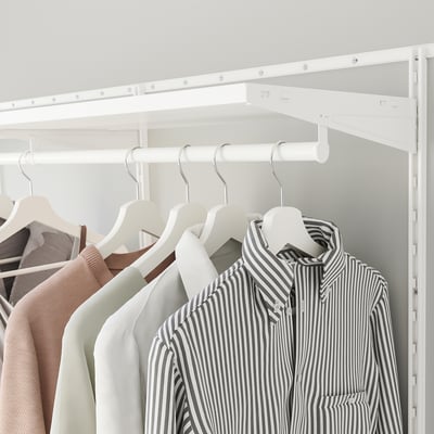 Un placard blanc avec des vêtements. Les chemises pendent soigneusement, y compris un chemisier rayé. Des rails et des étagères sont montrés, ce qui facilite l’organisation du rangement.