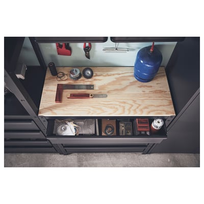 Étagère inférieure avec des outils sur un établi noir, avec un dessus en bois.