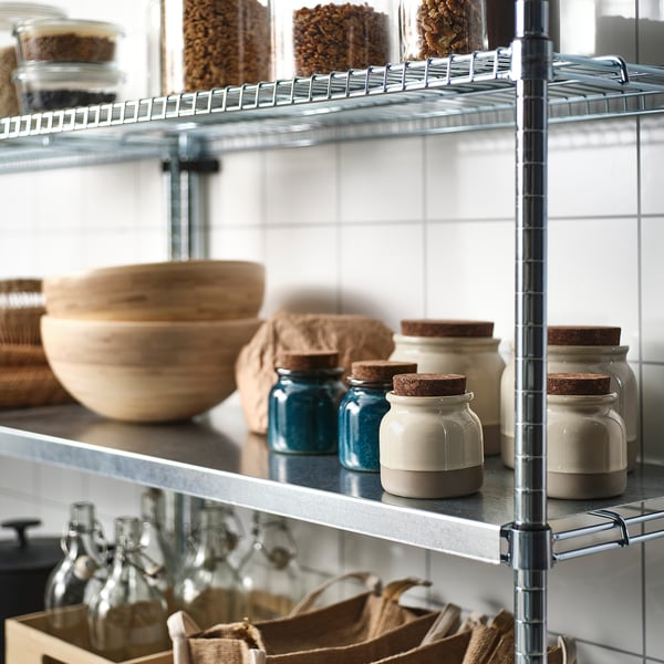 Étagères métalliques contenant des bocaux avec des couvercles en liège et des dessus bleus, des bols en bois, des sacs en tissu et des bouteilles en verre.