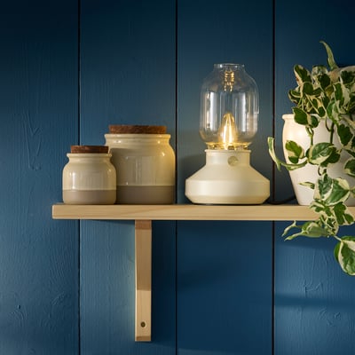 Étagère en bois avec pots en grès rugdahyj, lanterne et plante. Bocaux petits, lanterne plus haute, plante plus large.
