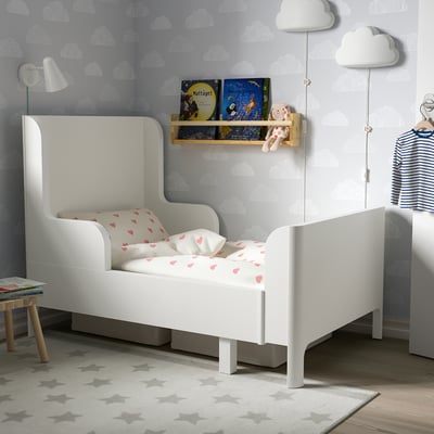 Chambre d’enfant avec lit élastique blanc, design arrondi, entourée de livres et de murs nuageux.