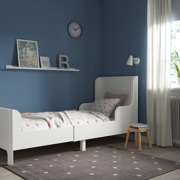 Lit d’enfant blanc dans la chambre bleue. Literie en forme de cœur, tabouret à côté, sous la fenêtre.