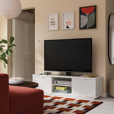 Salon moderne avec meuble TV blanc, téléviseur à écran plat, canapé rouge, tapis coloré et œuvres murales.