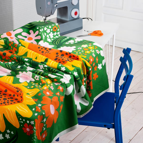 Tissu vif avec tournesols sur machine à coudre, prêt pour un projet créatif. Chaise bleue à côté de la table.