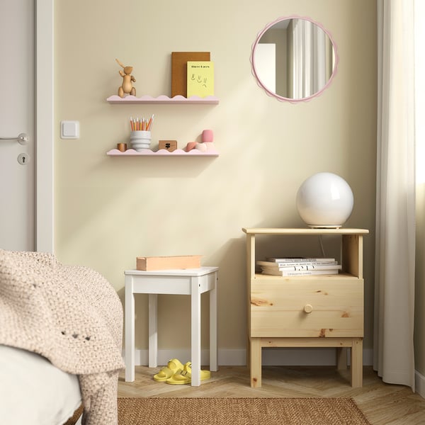 Coin confortable : miroir rose tendre sur table de chevet en bois, lampe, livres, couverture rose, chaussure jaune solitaire.