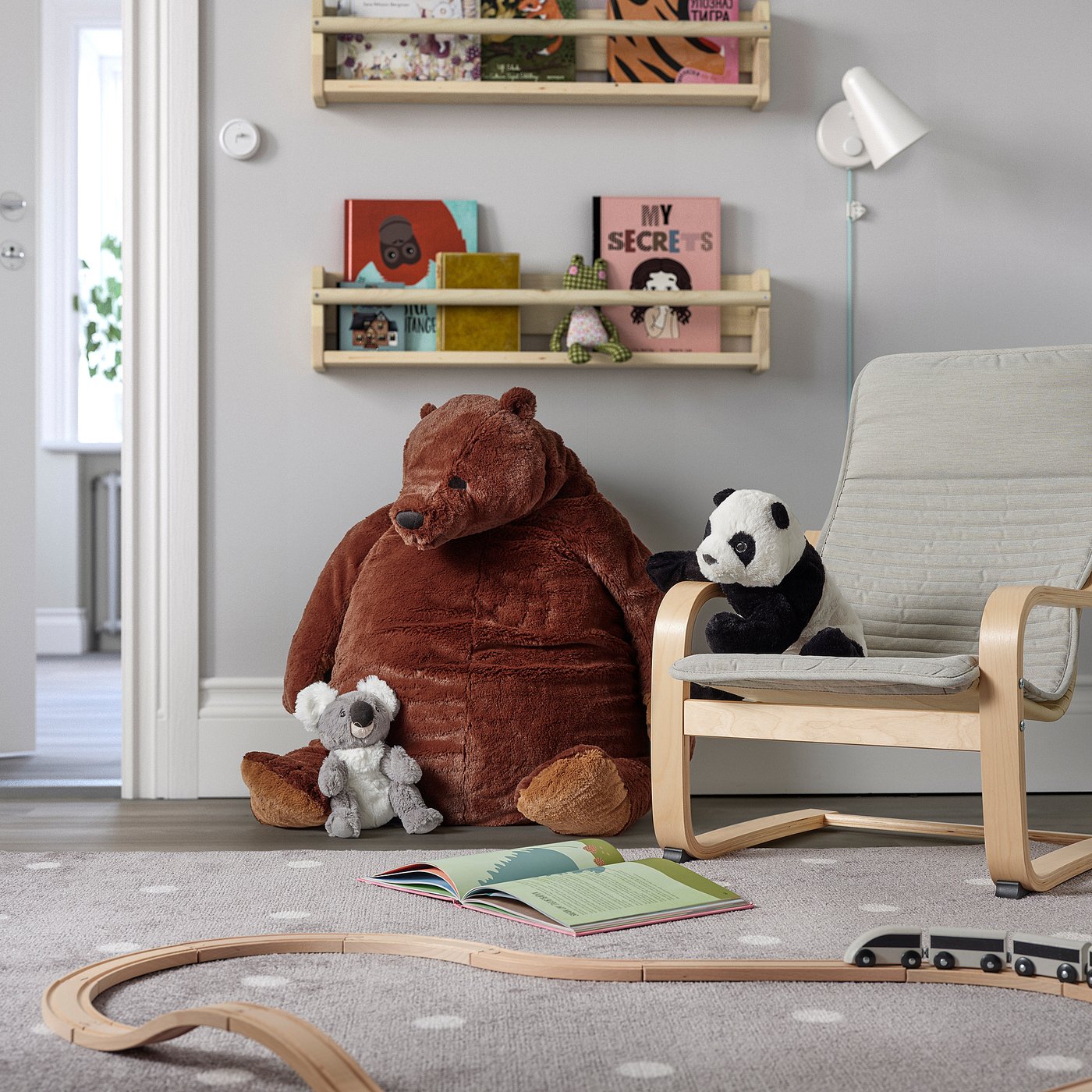 Jouet ours brun par étagère avec panda, chaise, livre et train.
