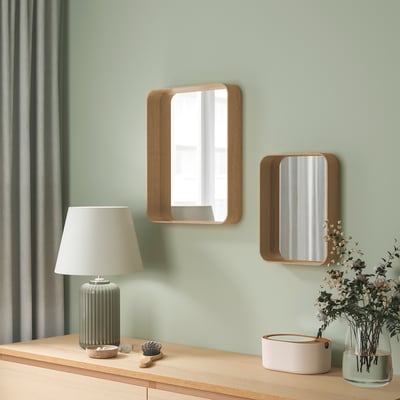 Deux miroirs encadrés en chêne sont accrochés sur un mur vert, une fenêtre réfléchissante, avec des décorations de table en dessous.