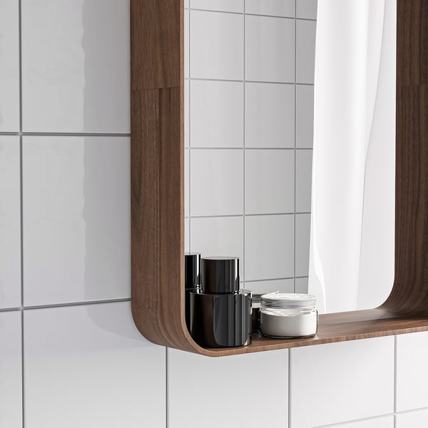 Miroir de salle de bain avec étagère en noyer, contenant une bouteille noire et un pot blanc.