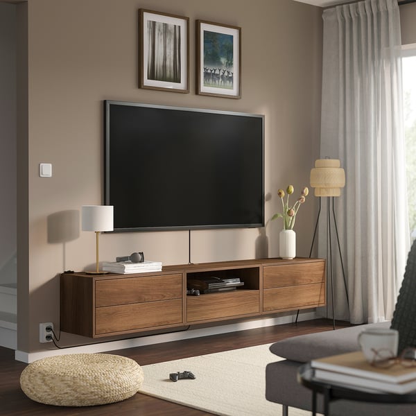 Salon moderne avec télévision murale sur l’unité EKET. Tiroirs, étagères et accessoires en bois. Rideaux légers, tapis et coussins.