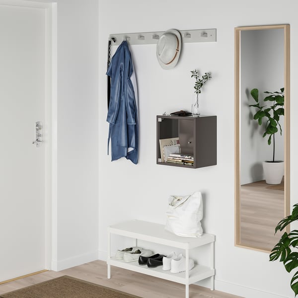 Petite porte en verre blanc pour présentoir cube EKET, s’insérant parfaitement au-dessus d’un banc dans une entrée bien rangée.