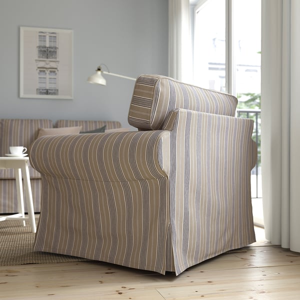 Un fauteuil rayé près d’une fenêtre avec un grand coussin de dosseret offrant un soutien dorsal.