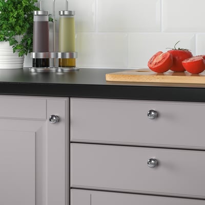 Armoires de cuisine modernes avec des boutons chromés et un comptoir noir, avec une planche à découper avec des tomates et des condiments en tranches.