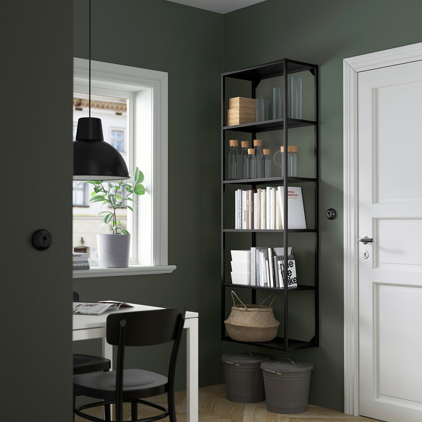 Bureau à domicile moderne avec étagère noire ENHET, contenant des livres et des vases. À côté d’un bureau blanc avec une chaise, une plante et une porte blanche.