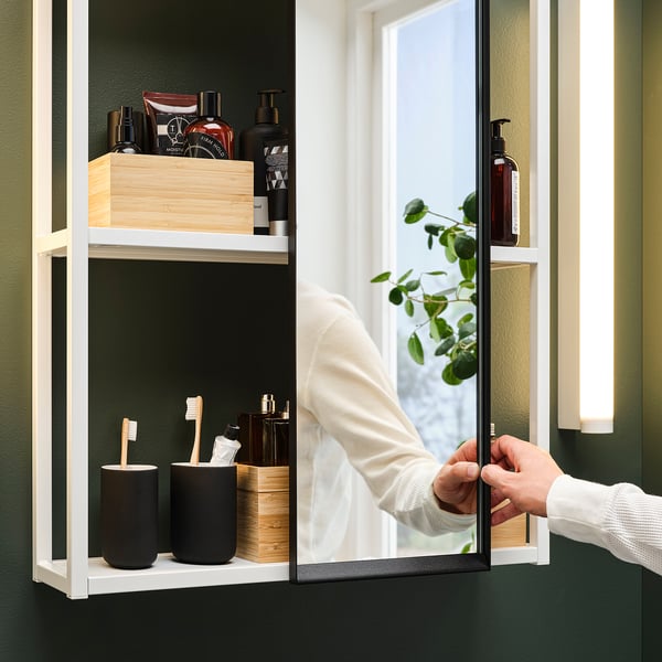 Personne ajustant l’armoire coulissante à miroir, révélant les articles de toilette et les brosses à dents.