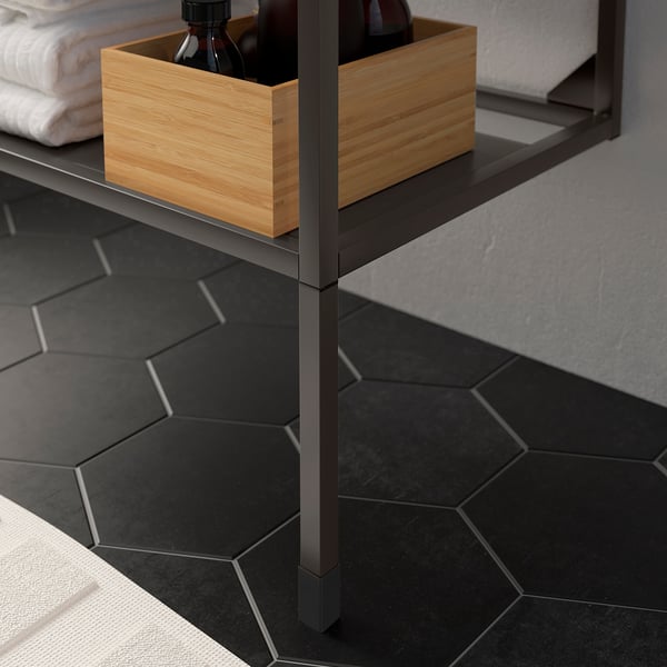 Étagère de salle de bain en métal noir avec des boîtes en bois. Les pieds réglables compensent les irrégularités du sol, comme le montre l’image.