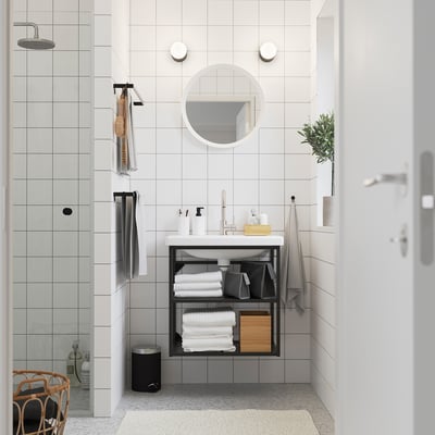 Salle de bain minimaliste : carrelage blanc, miroir rond, meuble-lavabo ENHET avec serviettes, boîte en bois, douche en verre, pomme de pluie, chaise en bois avec des vêtements.