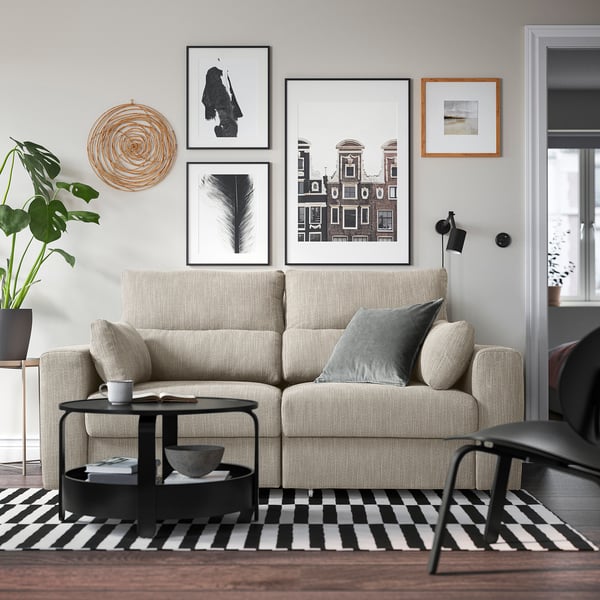 Salon moderne avec canapé beige, oreillers, table basse noire et art mural. Spacieux et relaxant.