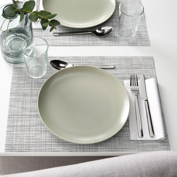 Deux couverts avec des assiettes, des verres, des couverts et des serviettes pliées sur des sets de table tissés, prêts à être dégustés.