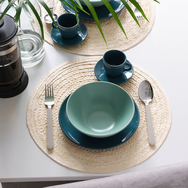 Une table avec des bols, des tasses et des sets de table tissés en FÄRGKLAR vert. Comprend des couverts et une presse à café.