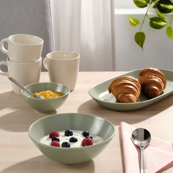 Table dressée avec des bols FÄRGKLAR remplis de yaourt et de baies, des croissants et des tasses pour un petit-déjeuner.