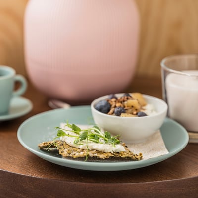 Assiette bleue avec de la nourriture verte, bol blanc avec du yogourt et des baies, sur une table en bois.