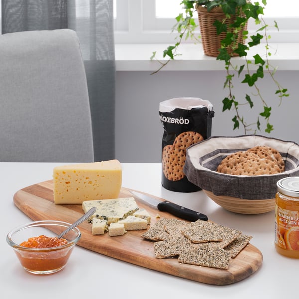 Planche à découper en bois avec du fromage, des craquelins, un couteau et de la confiture sur la table à manger, utilisée pour servir de la nourriture.
