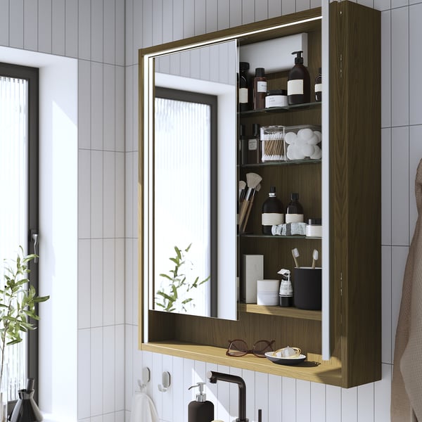 Armoire de toilette de salle de bain moderne avec éclairage intégré, rangement des articles de toilette, avec une finition en bois et une étagère, montée sur un mur carrelé.