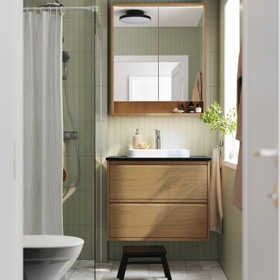 Meuble de toilette en bois avec lumières, vanité en bois clair au-dessus et douche en verre givré.