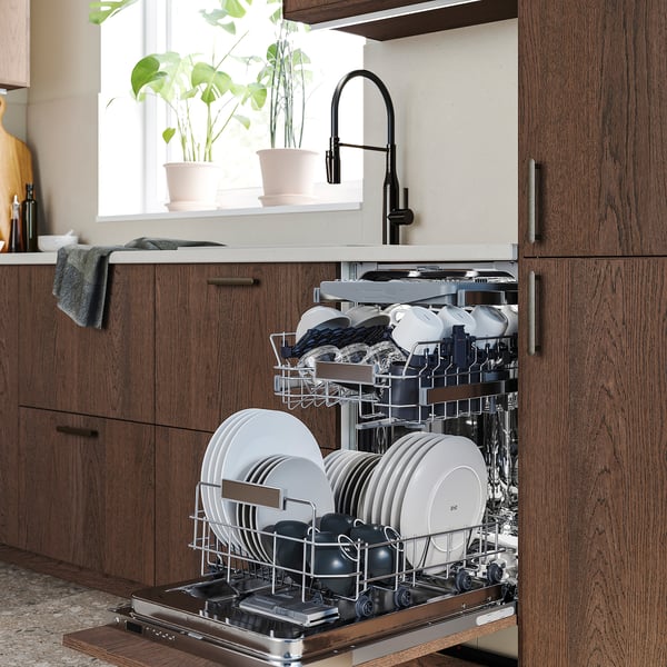 Lave-vaisselle avec vaisselle propre près de la fenêtre de la cuisine, lumière vive, plantes vertes.