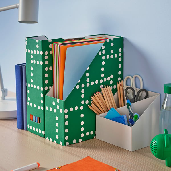 Porte-magazine vert à pois avec des dossiers colorés, un petit organiseur blanc, une bouteille bleue et une sphère verte.