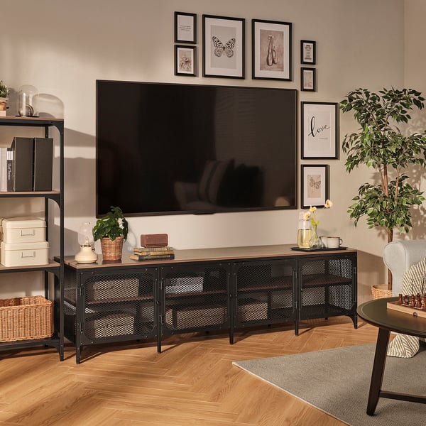 Salon moderne avec meuble TV FJÄLLBO en noir, pouvant accueillir une télévision grand écran. Entouré de parquet, d’objets décoratifs et de plantes.