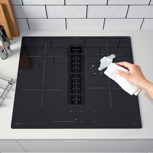 Une personne nettoyant une plaque à induction noire moderne avec 4 zones et une évacuation centrale.