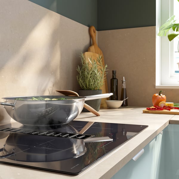 Cuisine moderne avec plaque à induction en acier inoxydable, cuisson de légumes verts, d’ustensiles en bois, de bouteilles et de produits frais.