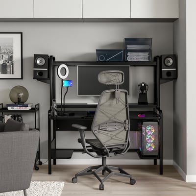 Configuration moderne de bureau à domicile noir avec un bureau élégant, une chaise en maille ergonomique et entouré d’appareils de haute technologie.