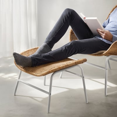 Personne allongée dans une chaise en osier, lisant un livre, les pieds reposant sur un repose-pieds assorti.
